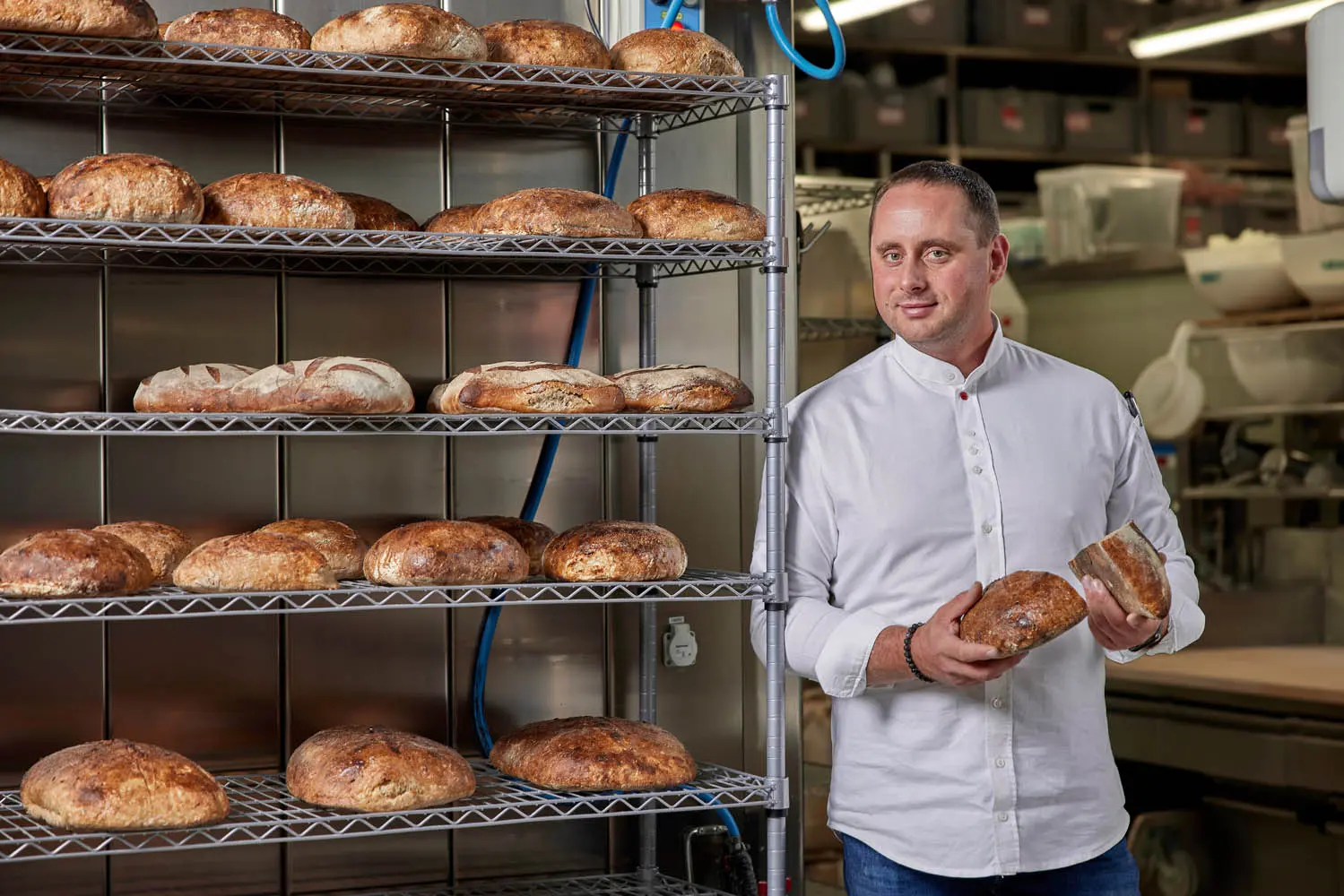 Baker from Eska Bakery holding freshly baked artisanal bread inside the bakery.